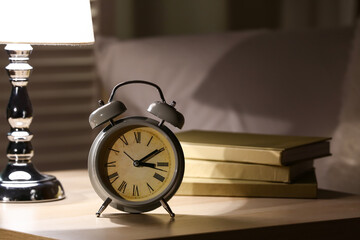 Alarm clock with lamp and books on table in bedroom at night