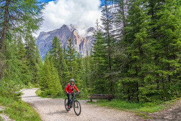 nice and active senior woman riding her electric mountain bike on the Pralongia Plateau in the Alta Badia Dolomites with awesome Sasso die Santa Cruce summit in Backg, South Tirol and Trentino, Italy