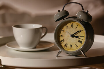 Alarm clock with cup of coffee on table in bedroom at night, closeup