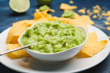 Bowl with tasty guacamole and nachos on color background, closeup