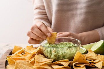 Woman eating tasty guacamole with nachos on light background