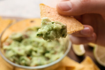 Woman eating tasty guacamole with nacho, closeup