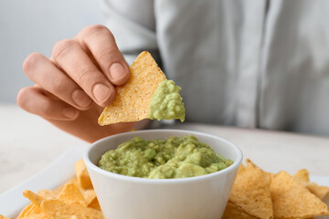 Woman eating tasty guacamole with nachos on light table, closeup