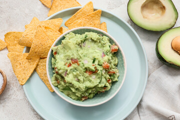 Bowl with tasty guacamole and nachos on light background