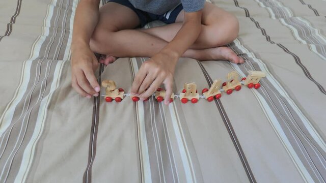 8 year old boy sat on the bed while he's playing with a train made of wood