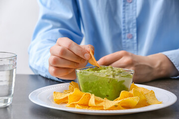 Woman eating tasty guacamole with nachos on dark table, closeup