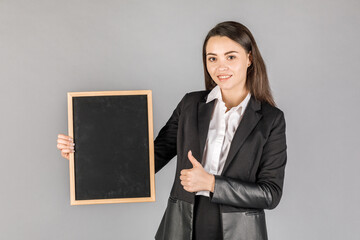 Young business woman in dark suite with black board in frame on grey background.