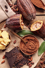 Composition with fresh cocoa fruits, beans, powder, butter and chocolate on wooden background