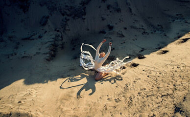 A girl in a white bodysuit in an open space among the sand.