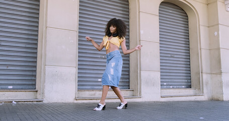 Fototapeta na wymiar Modern style dancer with afro on her head dancing on street