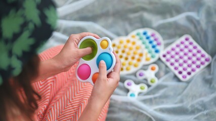 Teen girl plays with anti-stress multicolored toys popit and simple dimple in the park on a summer day.