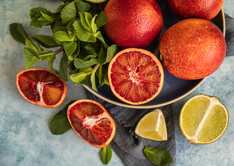 Whole and cut in half blood Sicilian oranges, limes and mint on blue concrete background. Top view.