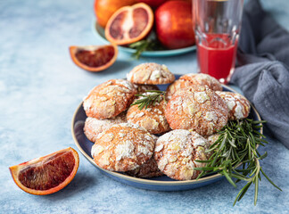 Homemade orange shortbread crinkle cookies with powdered sugar, rosemary and Sicilian blood oranges on blue concrete background.