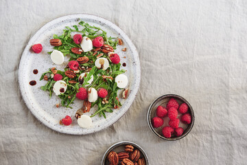 Fototapeta na wymiar Summer salad with arugula, raspberries, mozzarella cheese and pecan nuts. Morning, breakfast, healthy food. Selective focus