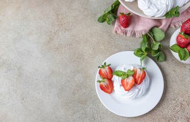 Mini Pavlova meringue cakes with strawberries and mint on a plate, concrete background. Top view.