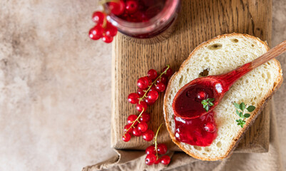 Slice of bread and red currant jam or jelly in a spoon, wooden cutting board. Top view.