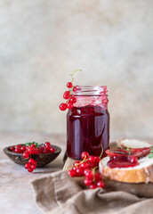 Slice of bread and red currant jam or jelly in a spoon, wooden cutting board.