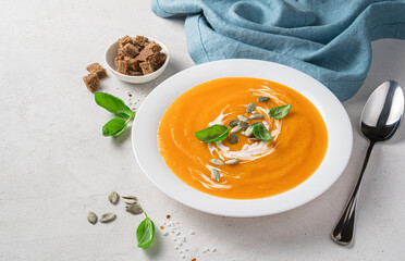 Autumn pumpkin cream soup with basil and cream on a gray background.