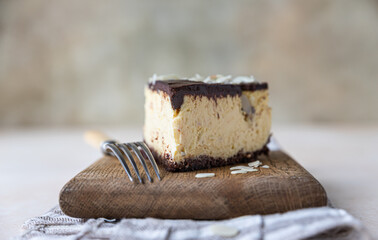 Slice of no baked creamy cheesecake with chocolate glaze and almond, light concrete background.