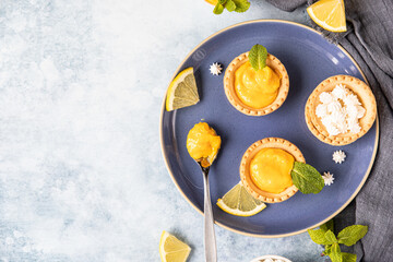 Lemon curd mini tarts decorated with mint and lemon slices on blue ceramic plate. Top view.