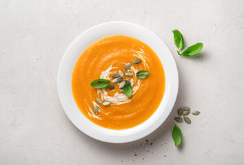 Pumpkin cream soup with basil, cream and pumpkin seeds on a gray background.