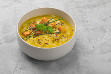 Organic vegetable puree soup with crackers, green onions and basil on a concrete background