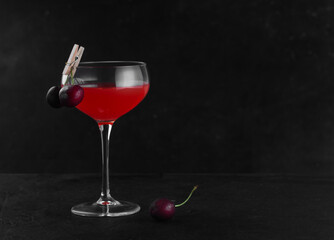 A glass with an alcoholic cocktail of red color and cherries on a clothespin