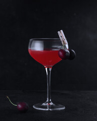 A glass with an alcoholic cocktail decorated with cherries on a clothespin