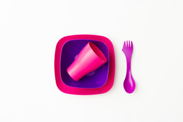 Purple plastic plates, cups, and forks and spoon on a white background
