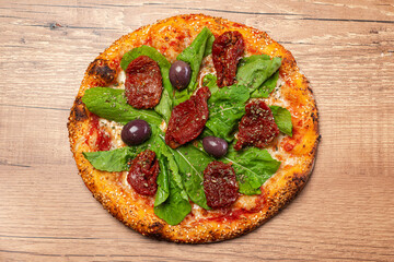 Sun-dried tomato pizza with arugula, gherkin and black olives, served over rustic wooden table.