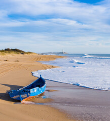 Immigrant and refugee dinghy boat stranded on the shore of a bautiful sand beach in south Spain. Coast of Cadiz in Andalusia with wooden boat washed by the shore waves © Pablo