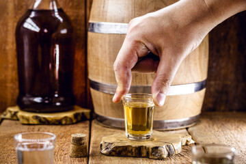 hand holding Brazilian distilled beverage, on rustic still background.