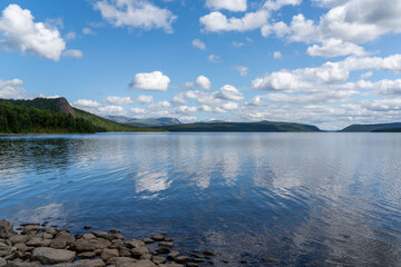 picturesque lake landscape with forest on the lakeshore and reflections of clouds and sky in the water