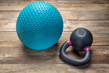 heavy rubber slam ball filled with sand and  small iron kettlebell on a rustic wood background, ...
