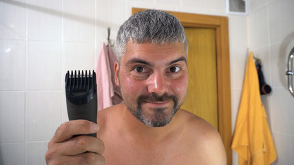 The man holds an electric razor in his hand. Facial care. Trimer. The man is preening. Positive...