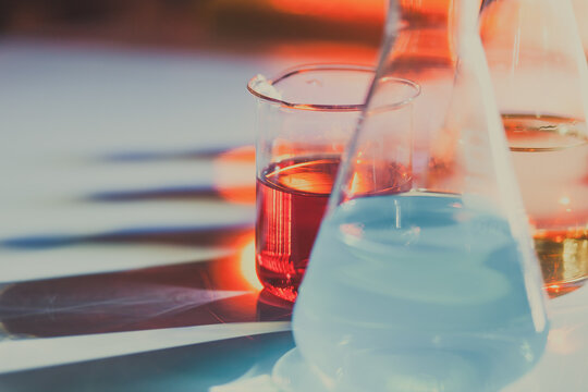 Illuminated laboratory flask filed with colorful chemical solutions with shadows on the table. Laboratory, science, chemistry... consept.