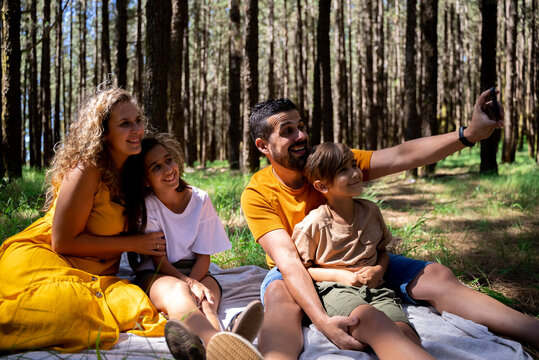 Happy young family resting together in woods and taking selfie picture with mobile phone camera.