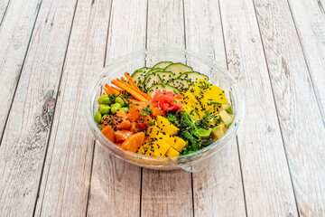 Salmon poke bowl with ripe avocado, edamame, red onion, grated carrot, diced mango, sliced raw cucumbers and wakame seaweed salad with sesame and poppy