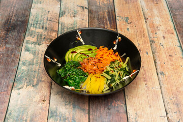 Marinated salmon poke bowl with ripe avocado slices, mango strips, green cucumber strips, wakame seaweed salad, carrots and sauces on white rice