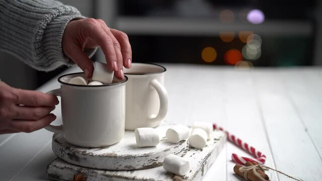 Woman throwing marshmallow into cocoa cup installed on wooden board