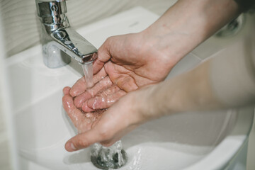 a man washes his hands under the tap in the bathroom