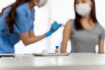 Close up coronavirus covid-19 vaccine bottle on clinic table with blur nurse or medical staff...