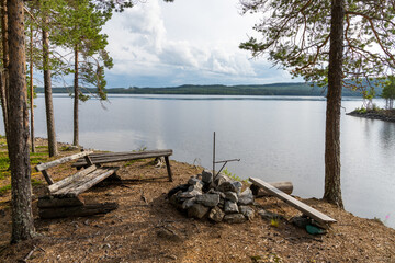 Fototapeta na wymiar wooden table and benches in the forest on the lakeside with a fireplace and grill in northern Sweden