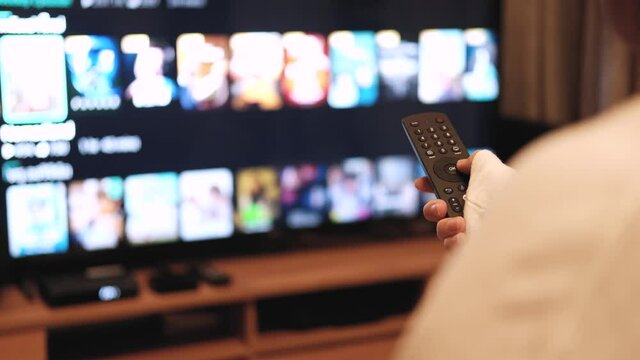 close up on the hand pressing the TV remote to select a movie or show to watch on TV. in the living room 4k