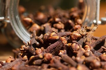 Dried clove seeds, in shallow focus, in front of a clear glass container