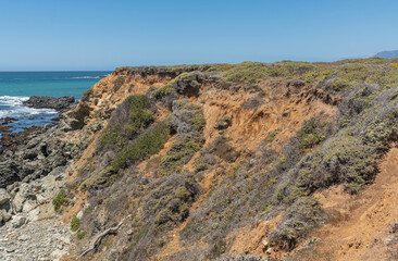 San Simeon, CA, USA - June 8, 2021: Pacific Ocean coastline north of town. Closeup of brown rocky...