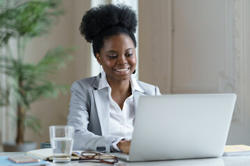 African businesswoman look on laptop screen with happy smile. Young ethnic office worker or boss...
