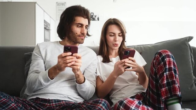 A smiling couple woman and man are looking social media content sitting on the sofa indoors