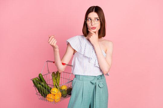 Photo of young girl hand touch chin think buy natural organic vegetables basket isolated over pink color background