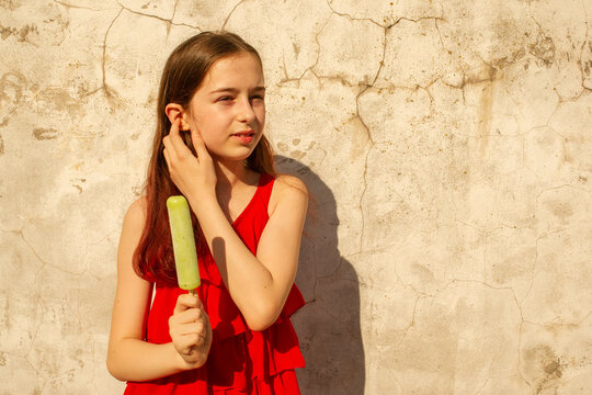A girl 10 or 11 years old on a hot sultry day in a red dress. Summer teenager girl with ice cream.
